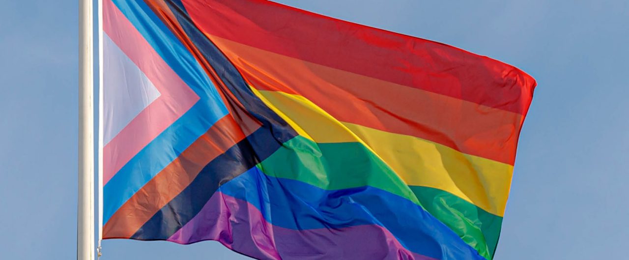 Progress pride flag (new design of rainbow flag) waving in the air with blue clear sky, Celebration of gay pride, The symbol of lesbian, gay, bisexual and transgender, LGBTQ community in Netherlands.
