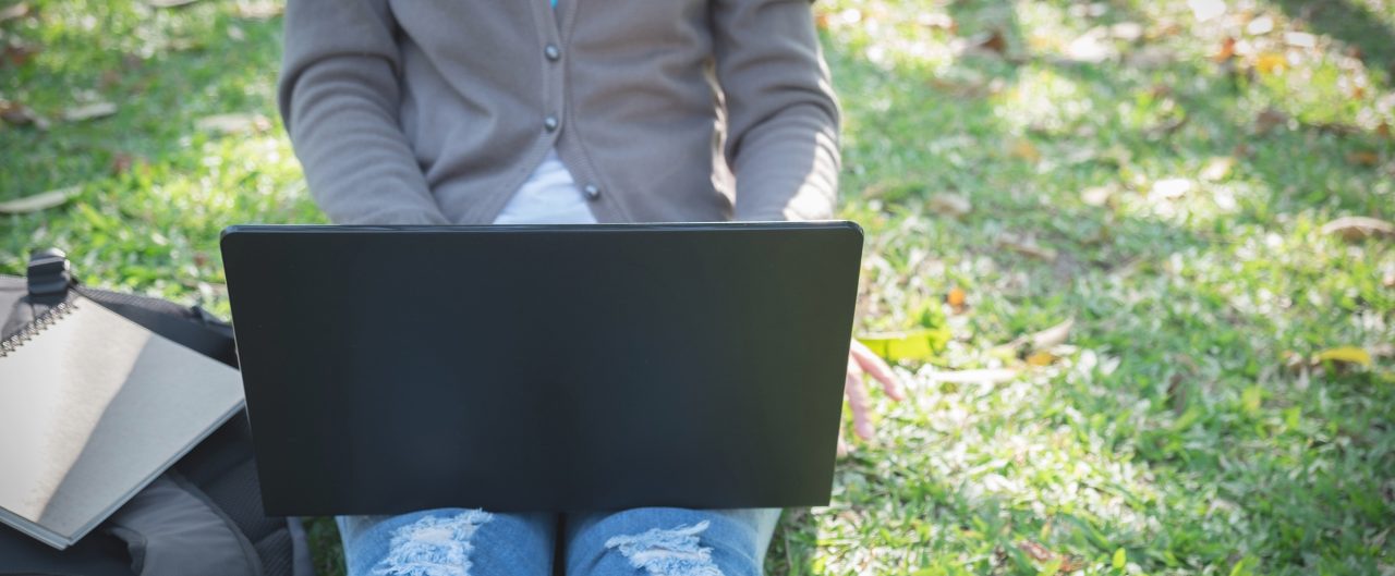 Laptop on the lap of a woman sitting on the lawn