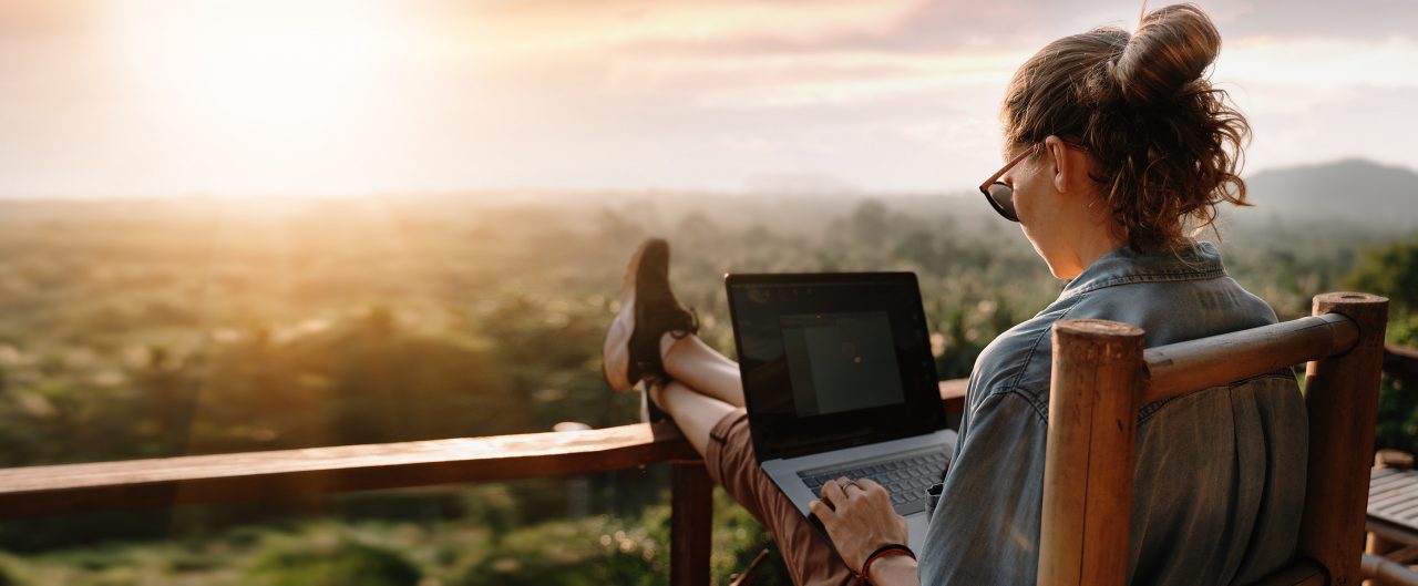 Young female working at a laptop at sunset or sunrise on the top of the mountain to the sea, working day.