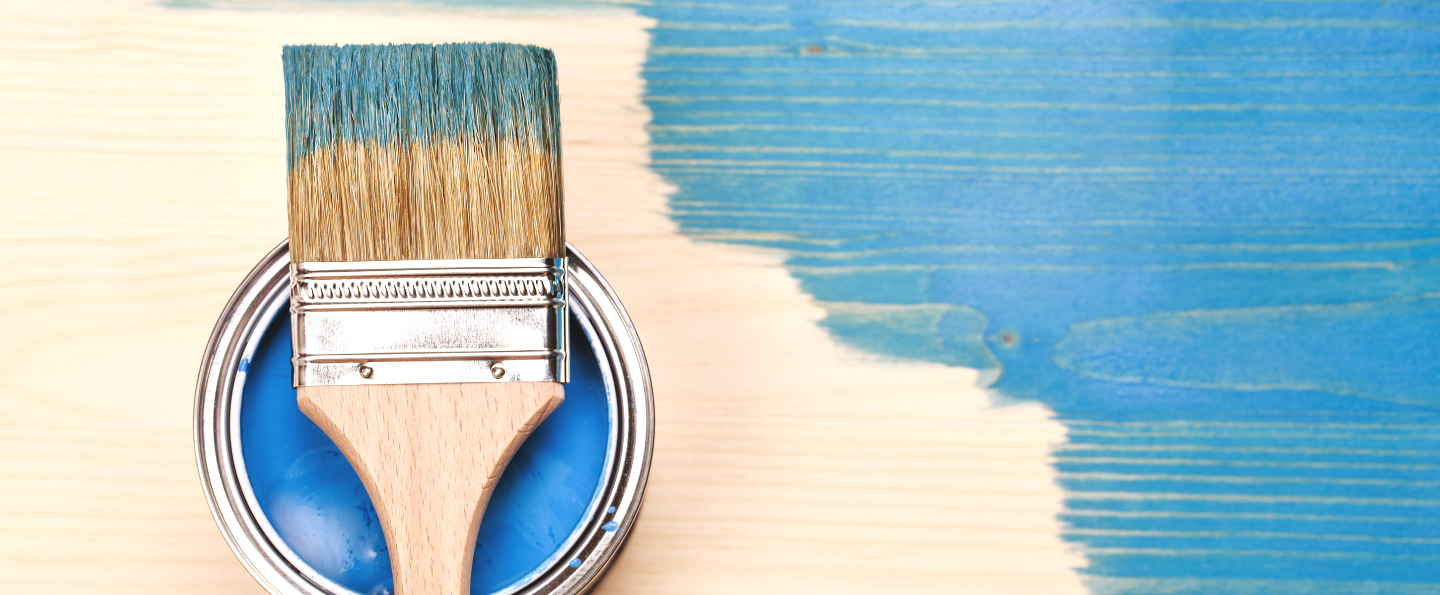 A paintbrush on a piece of wood that is incomplete but painted half blue.