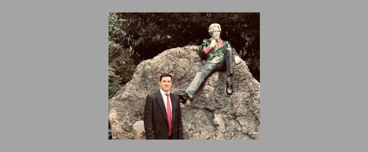 Man in suit standing next statue of a man sitting on a boulder