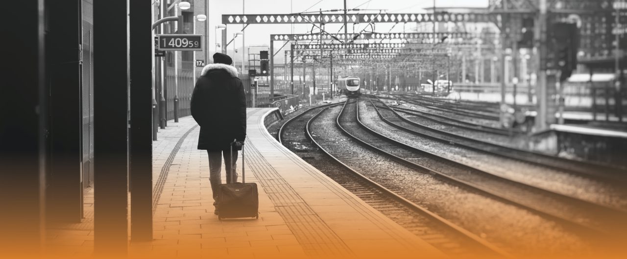 Black and white image of a man pulling his hand luggage across a train platform