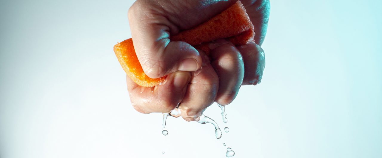 male hand squeezes a sponge for washing with water and drops fall down concept on a light blue background
