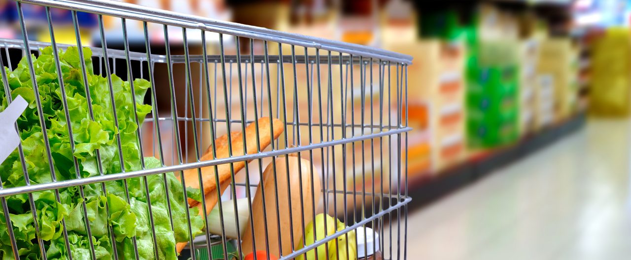 Shopping cart full of food in the supermarket aisle. Side tilt view. Horizontal composition