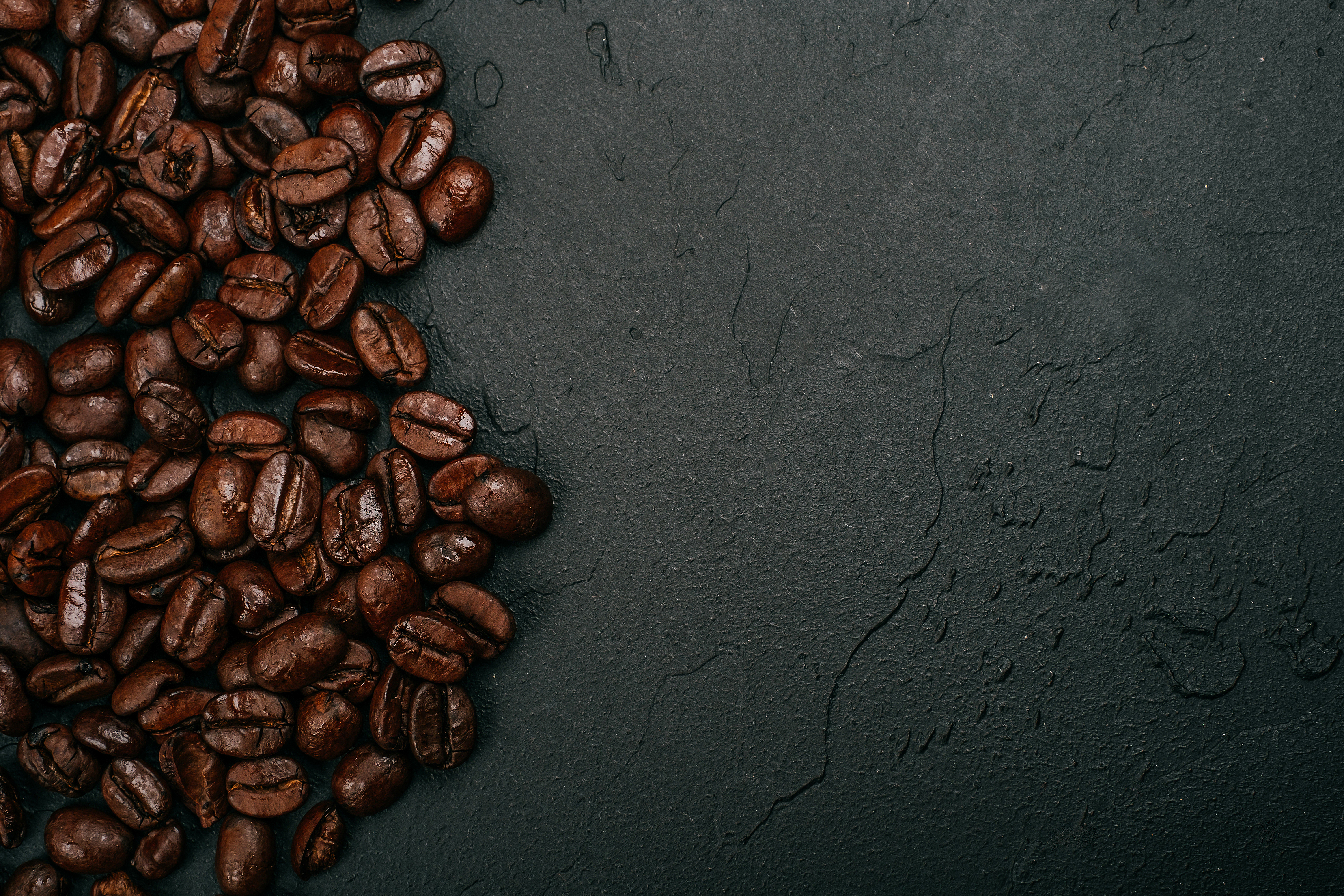 Roasted brown coffee beans on the black concrete stone background. Flatlay style, messy pattern.