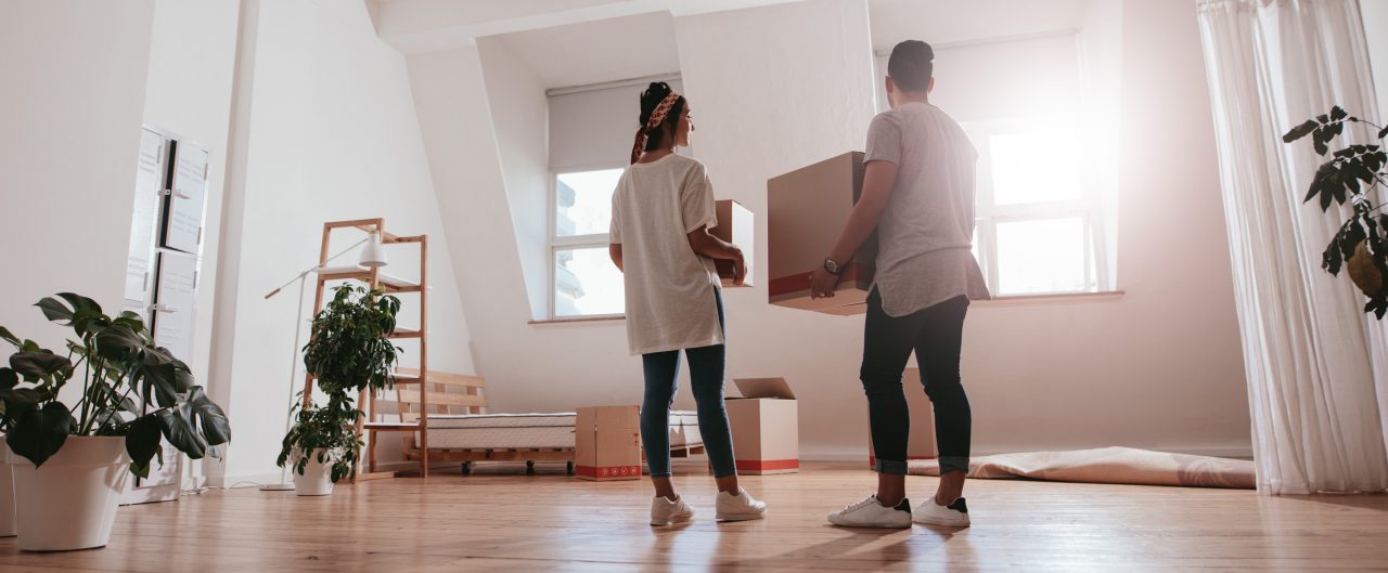 Young man and woman holding boxes and moving in new house.