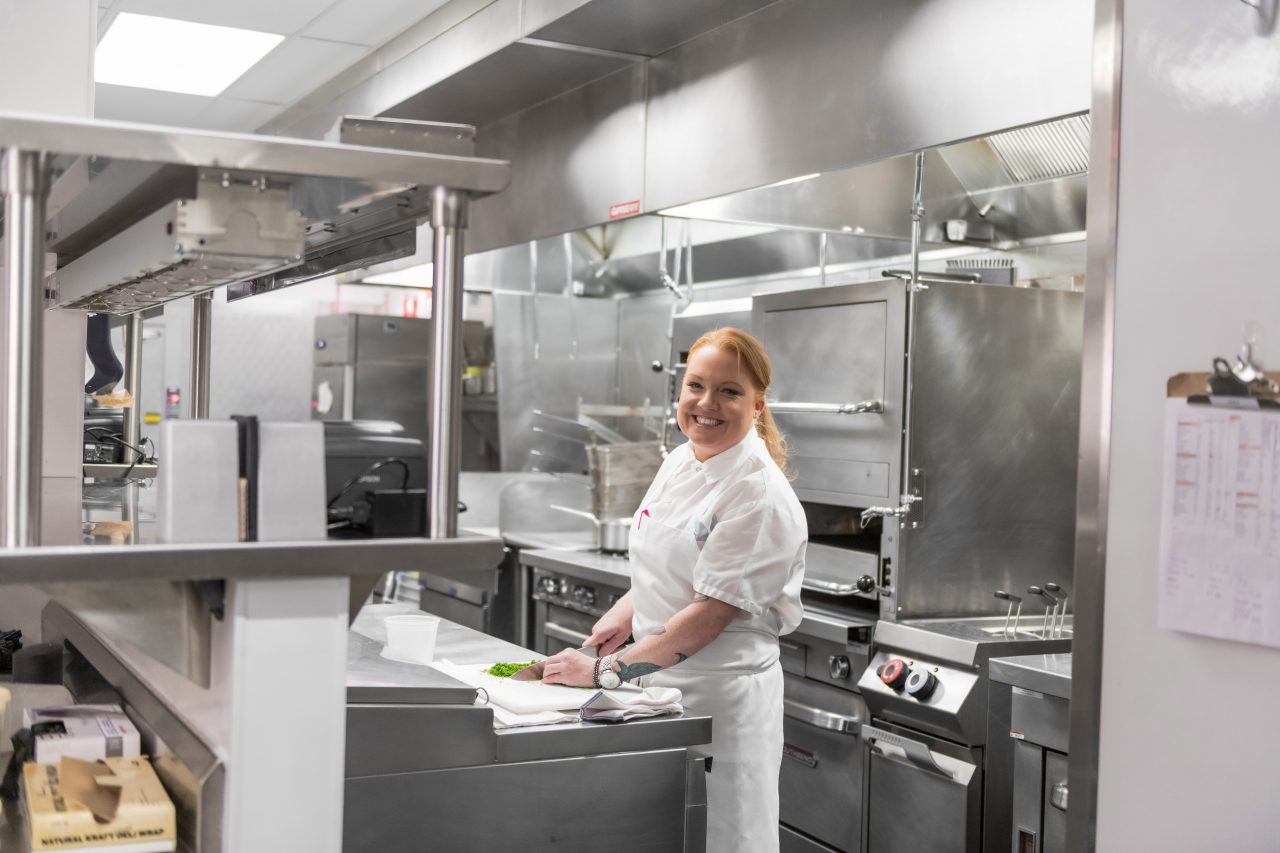 A female chef smiles as she cuts up greens with a knife