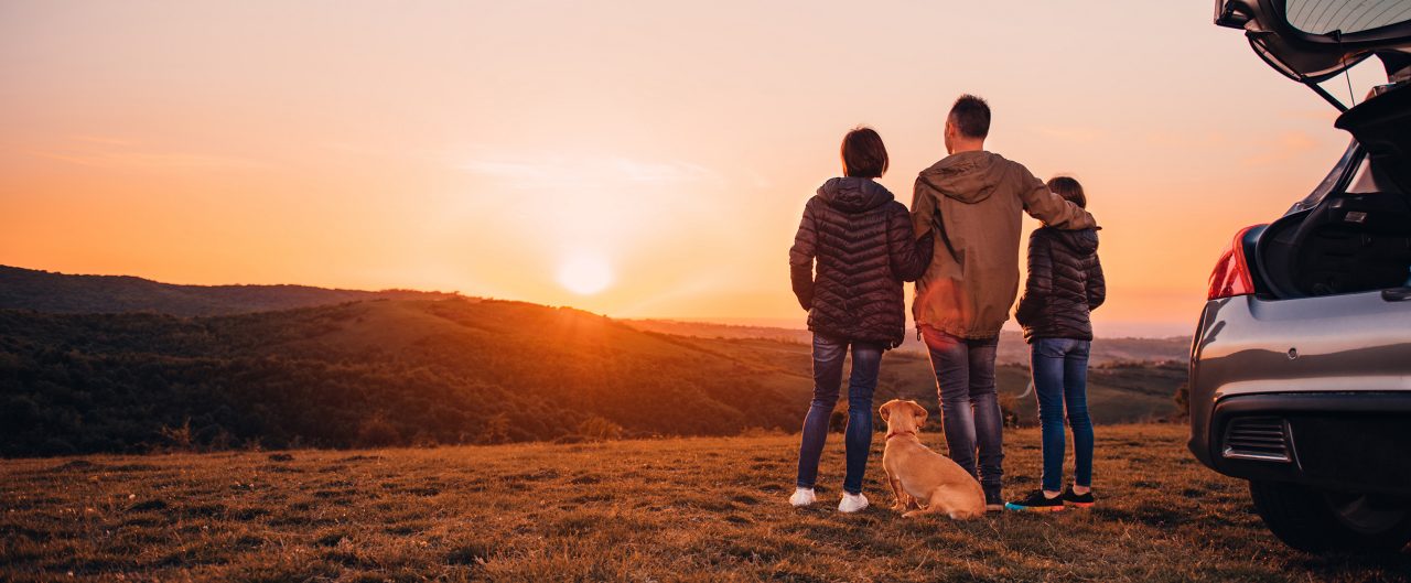Family with small yellow dog embracing at hill and looking at sunset