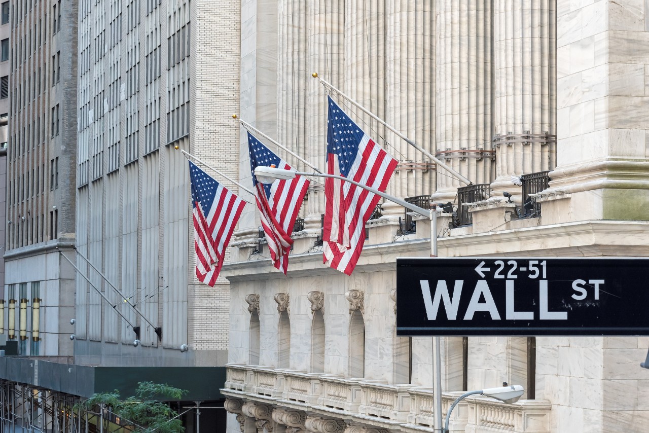 Wall Street sign with American flags and New York Stock Exchange in New York City