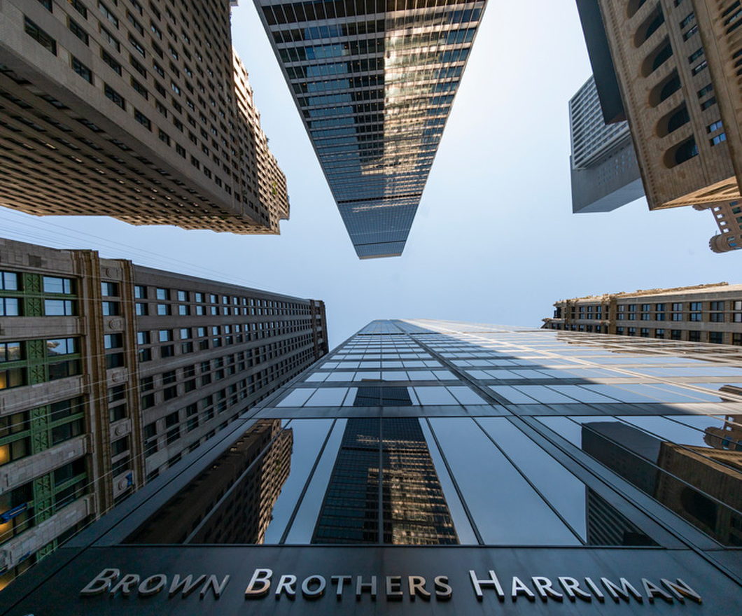 Brown Brothers Harriman building taken from down below with skyscrapers surrounding and a clear blue sky