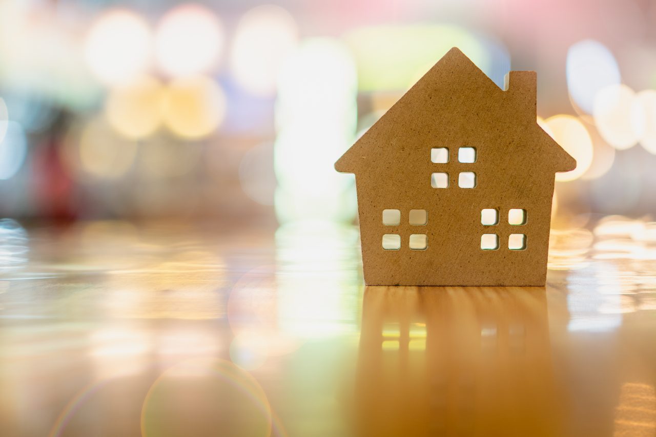 Miniature wood house on a wood table with bright lights in background. 
