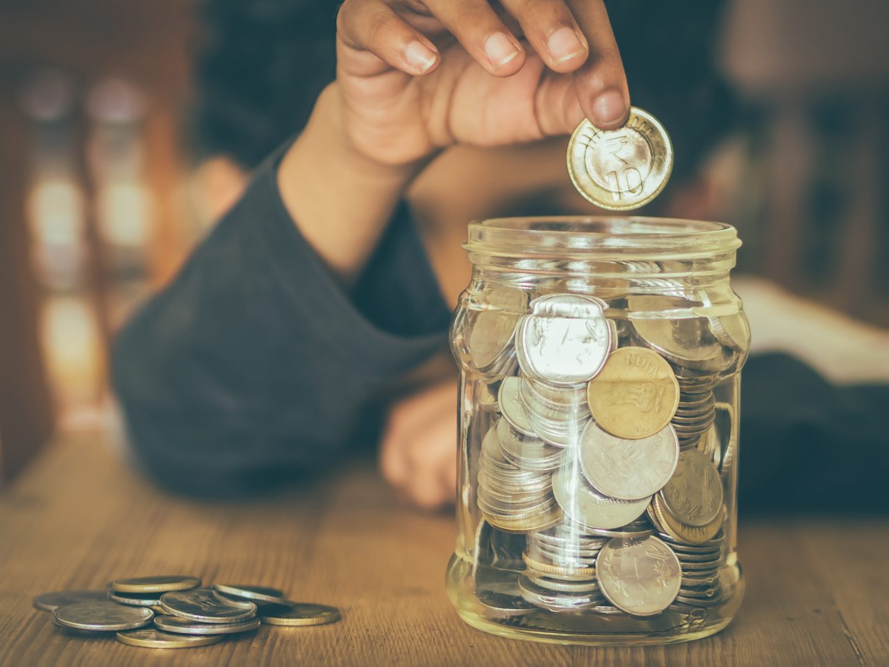 Yound child putting coins into a mason jar for savings.