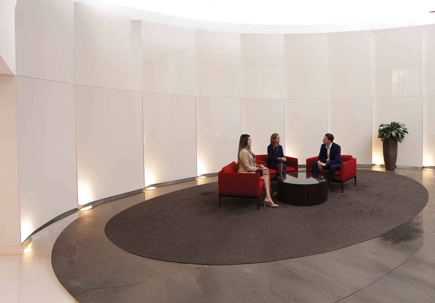 Two women and one man seated in lobby talking with each other