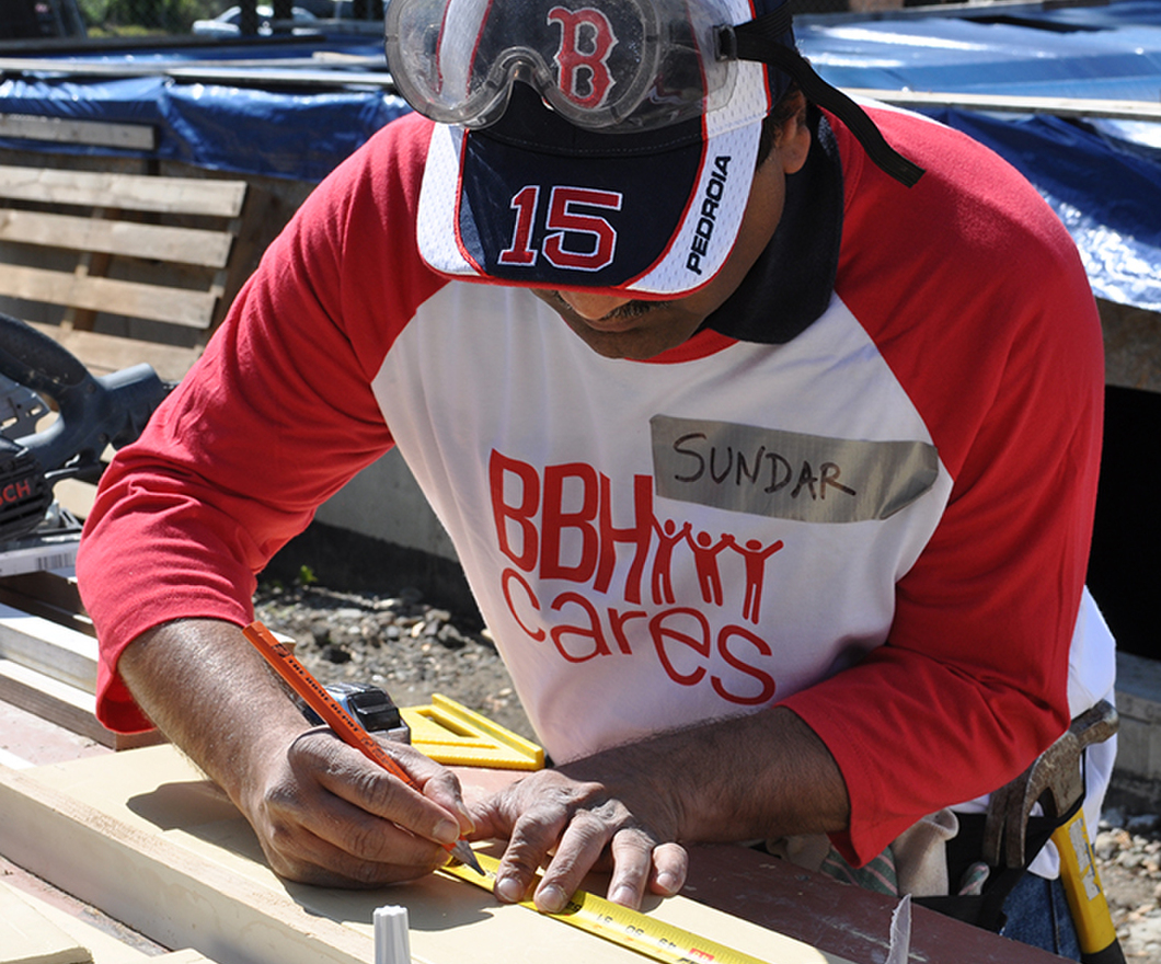 Sundar, a BBH'er using a tape measure while volunterring in his BBH Cares t-shirt and Red Sox hat with safety goggles on his head. 
