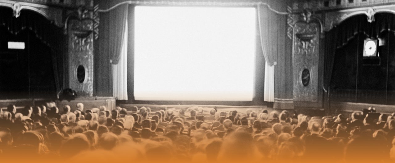 Black and white image of an old theatre showing the crowd and screen