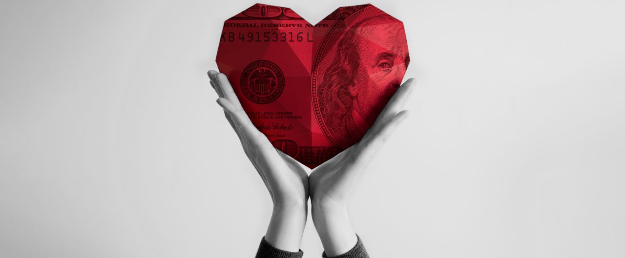 Two female hands holding red polygonal currency paper heart shape. 