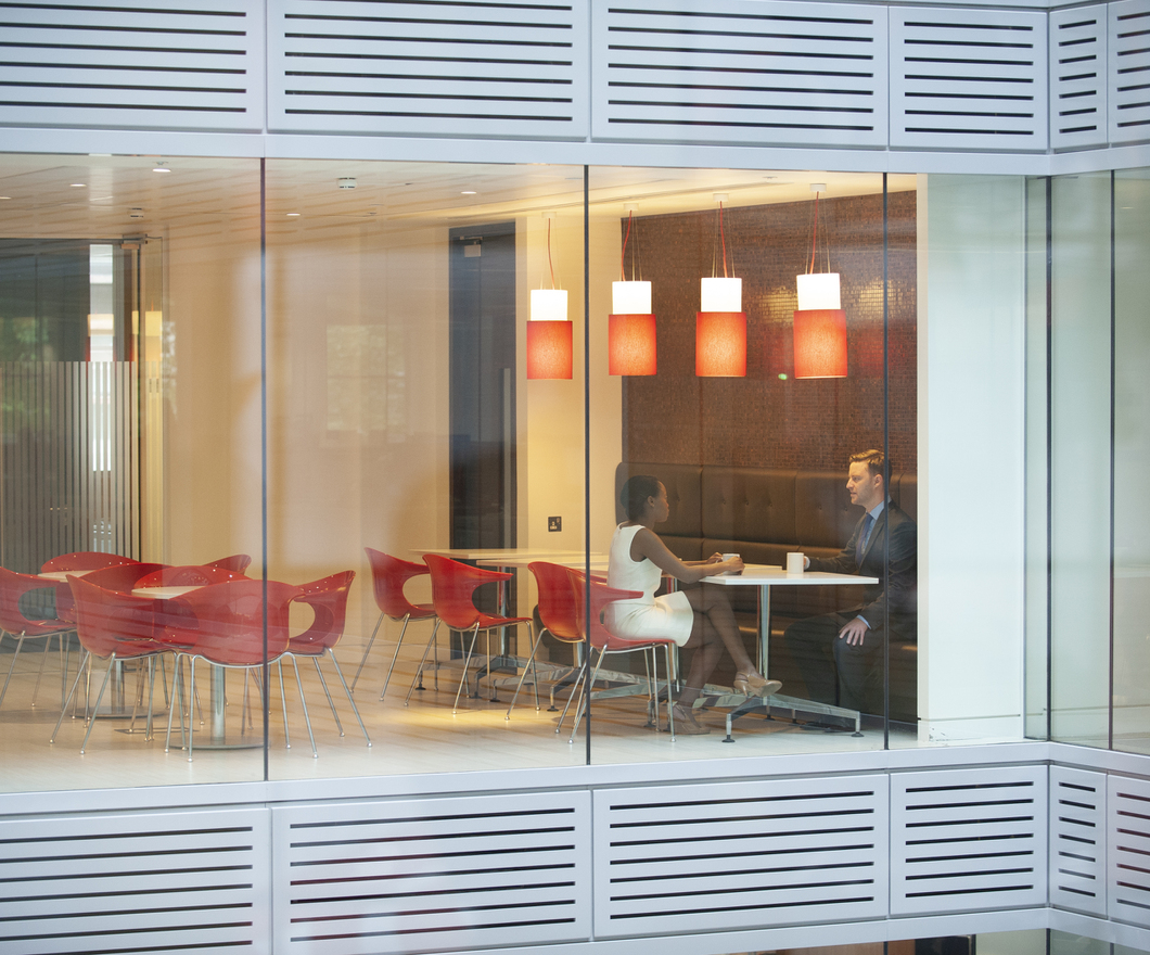 2 BBH'ers Visible Through Glass Walls Sitting at a White Table