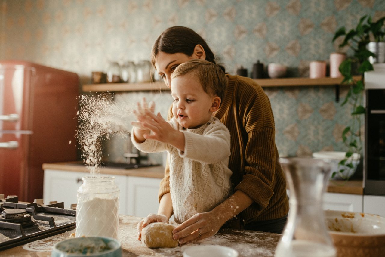 Mother and son are preparing dough with kid throwing flour in the air