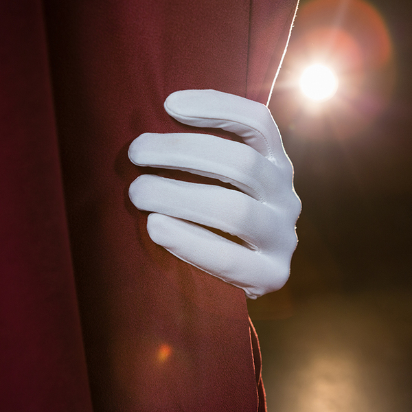 Close-up of hand in a white glove pulling red curtain away