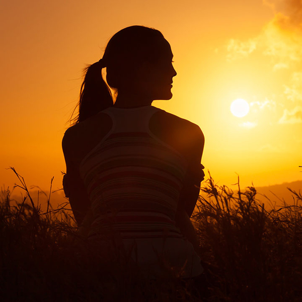 Woman sitting and looking out into a field of grass during sunrise.