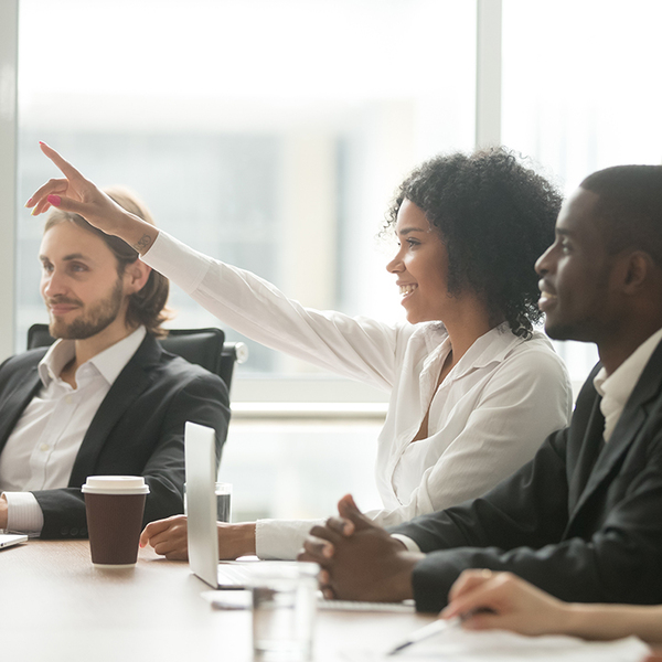 African American woman raises her hand to ask question during team meeting.