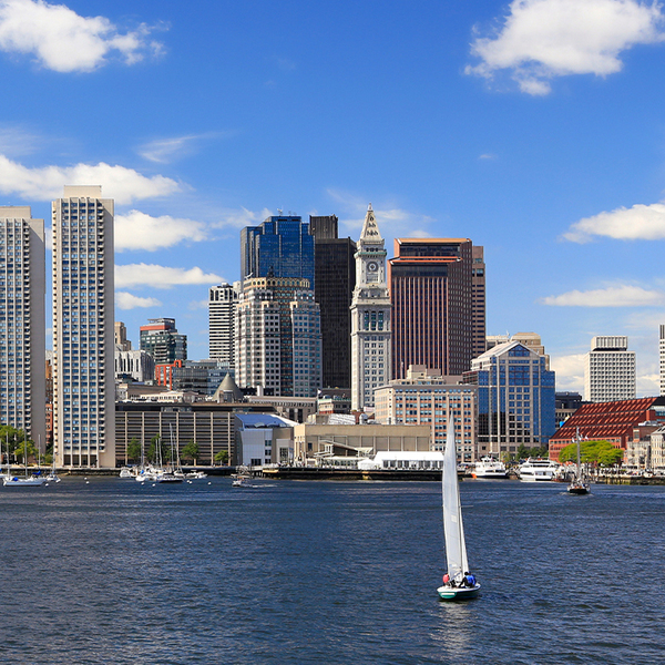 Boston city skyline seen behind a body of water with a sailboat in the center of the image