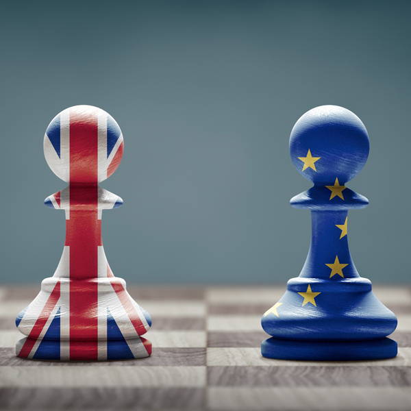 Two chess pieces one with UK flag and one with EU flag facing eachother on a chess board.