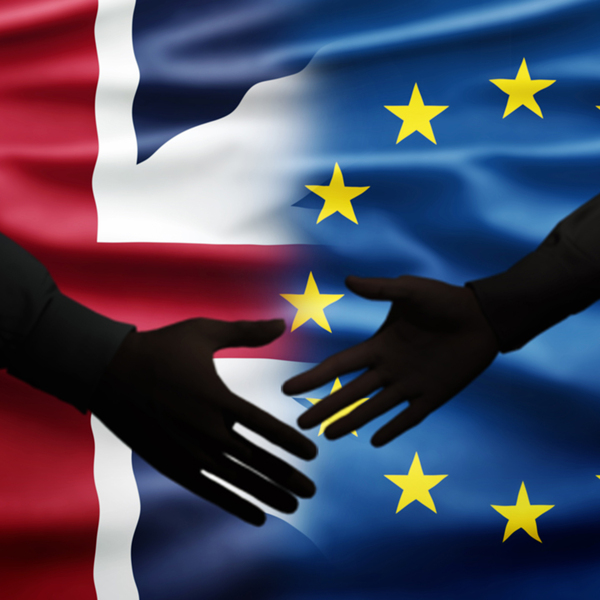 Two men shake hands in front of British flag and European flag