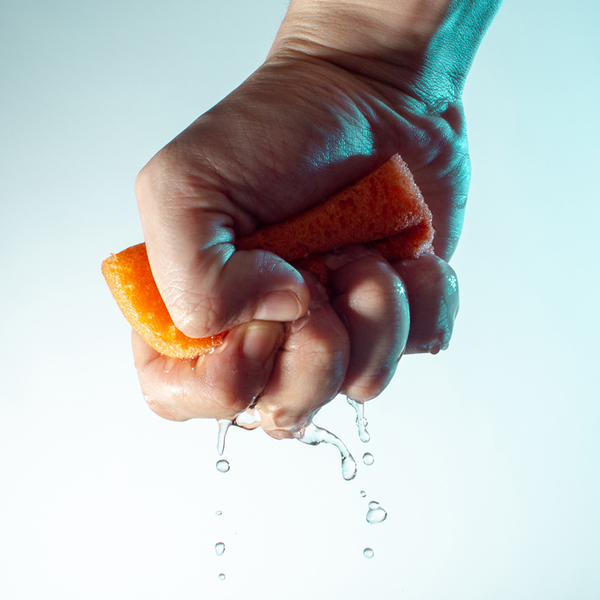 male hand squeezes a sponge for washing with water and drops fall down concept on a light blue background