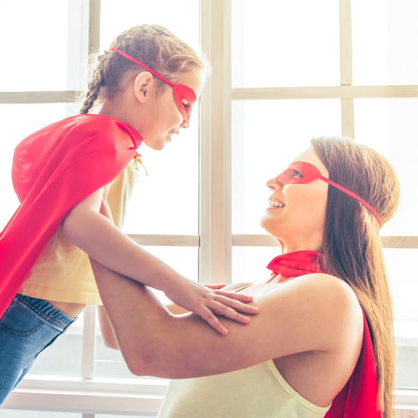 Mom holding up daughter as both wear superhero masks and capes