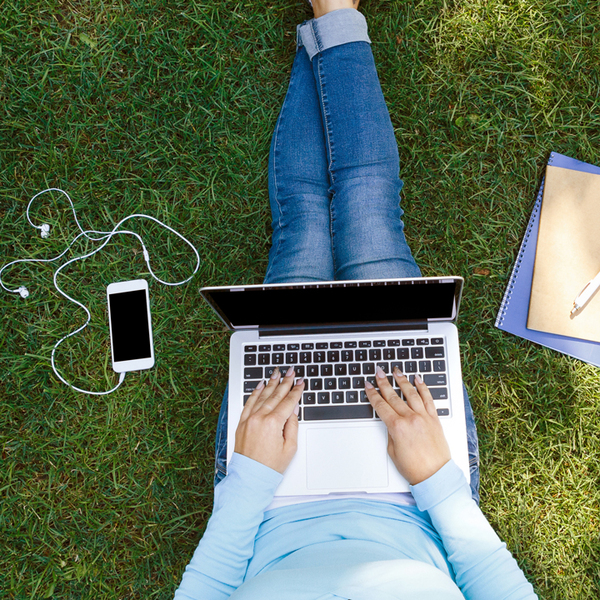 Top view of girl sitting in park on the green grass with laptop, notebook and smartphone with earphones,