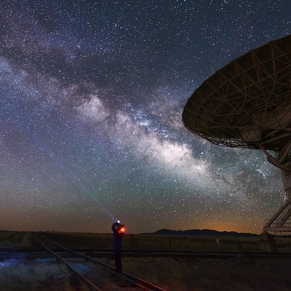 Big antenna disk and person looking through telescope at starry night sky 