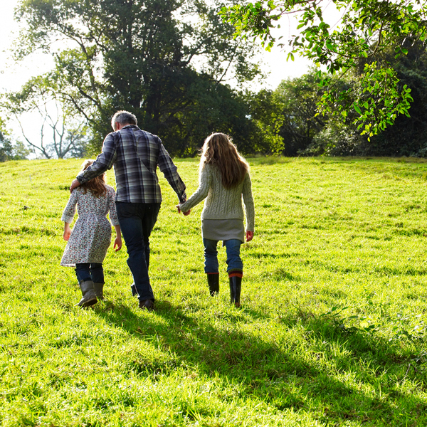 Photo of adult woman walking in nature and holding hands with two children.