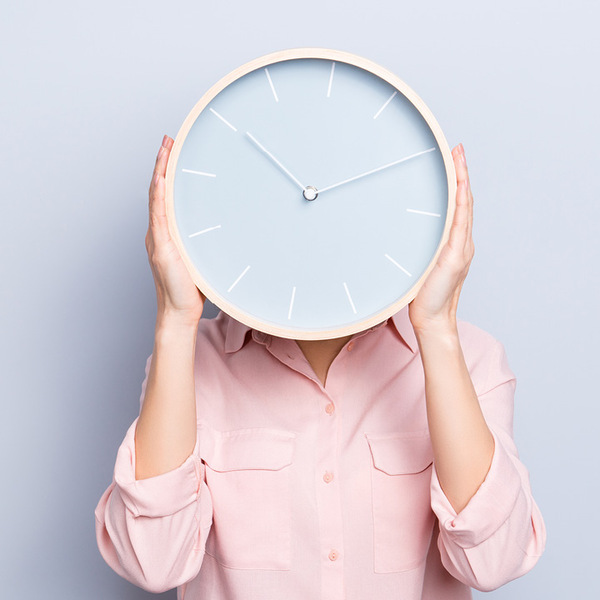 Woman holding a clock in front of her head.