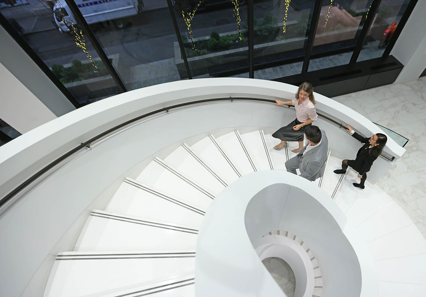 A woman, a man, and another woman walking up an internal spiral white staircase