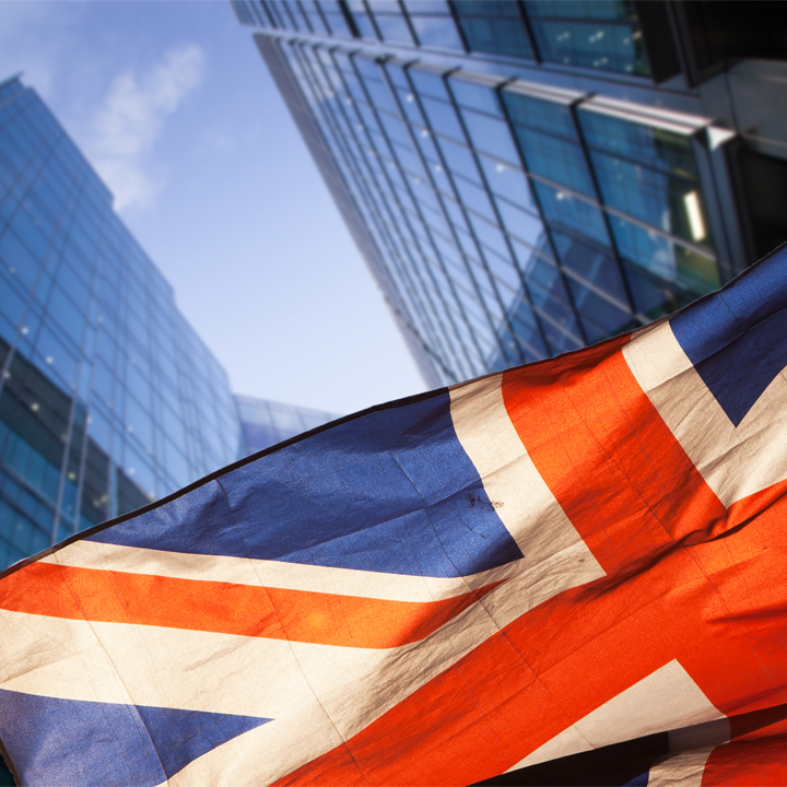 UK Flag flying in wind with skyscrapers behind it