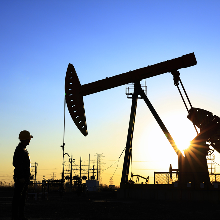 Oil worker and oil pump silhouette with yellow and blue sky behind them