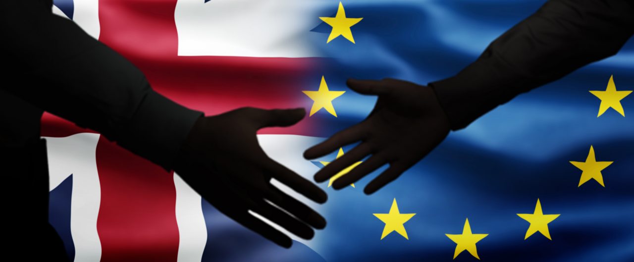 Two men shake hands in front of British flag and European flag