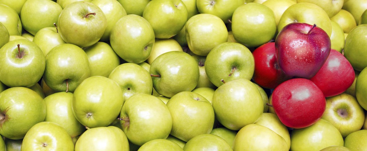 Huge pile of green apples, with 4 red apples placed on the top