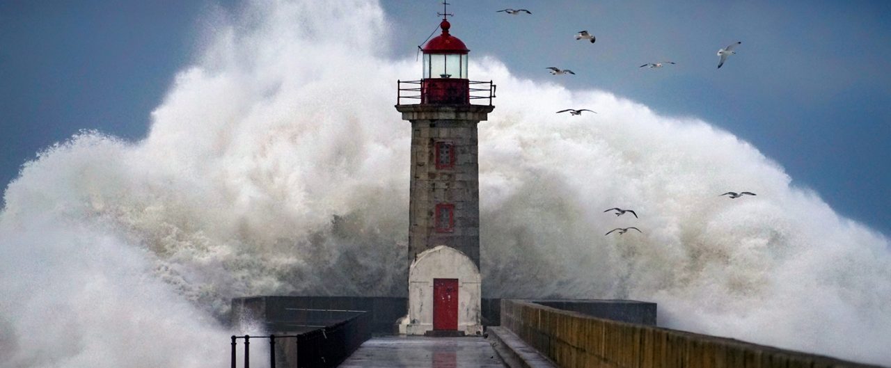 Large wave crashing behind a lighthouse