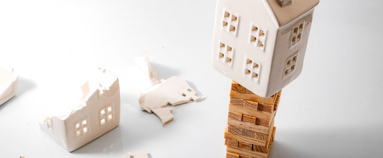 Financial risk, unstable real estate investment and shaky housing market concept with a home on stacked wooden building blocks surrounded by the ruins and debris of another house that collapsed