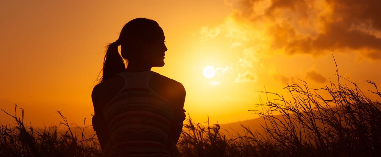 Woman sitting and looking out into a field of grass during sunrise.